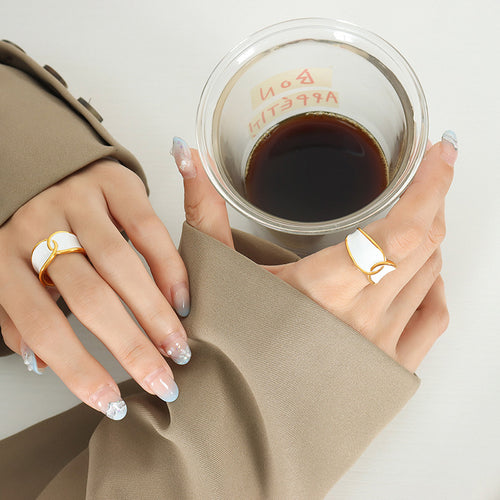 Two hands wearing white enamel gold geometric open rings by coffee cup