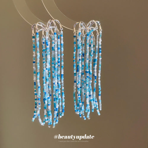 Styled view of blue bead tassel stud earrings with silver tone chains
