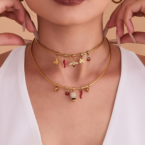 Model wearing layered gold snake chain charm necklaces with bee and bell