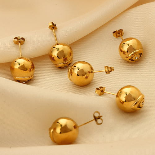 Multiple gold evil eye ball stud earrings on cream fabric