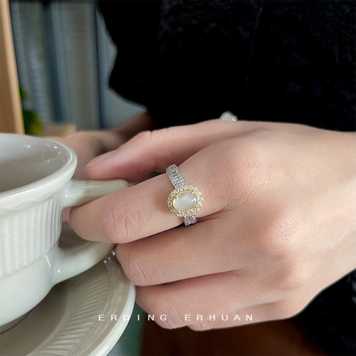 Two-tone oval halo ring worn on hand with coffee cup