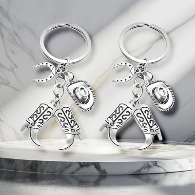 Two silver cowboy boot hat horseshoe keychains on marble podium