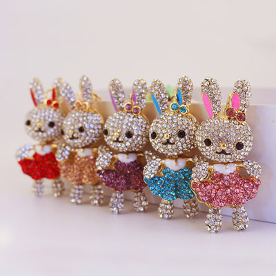 Five rhinestone rabbit charms stand in a row wearing red, peach, purple, blue, and pink dresses.