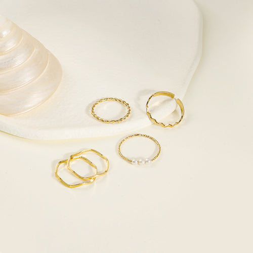 Gold thin rings including pearl and twist styles on cream surface