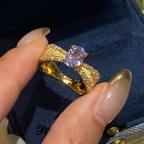 Close-up of gold textured ring with purple oval stone held over blue velvet