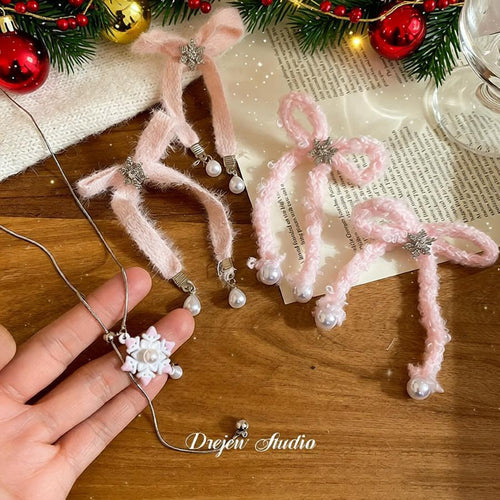 Hand holding silver snowflake pearl necklace beside pink bow pieces