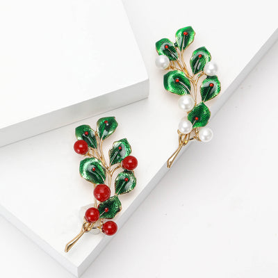 A slim gold tone branch set with red and green stones shown on a white background.