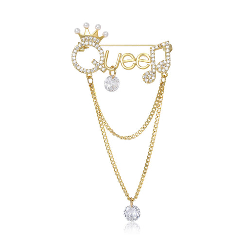Front view of the queen chain dangle brooch showing gold-tone Queen lettering with clear stones, draped chains and a cry