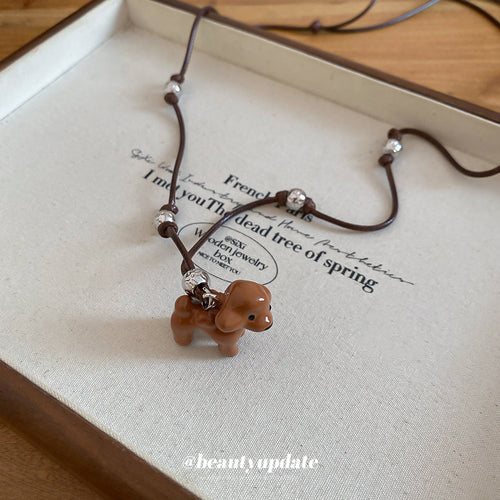 A small glossy brown dog-shaped pendant on a fine black cord shown in a styled close-up
