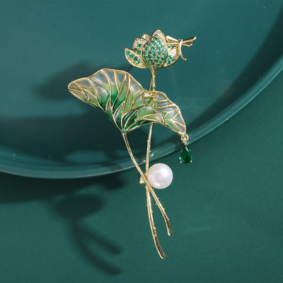 Display view of green lotus leaf brooch with flower bud and dragonfly standing on white blocks.
