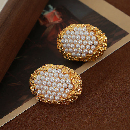 Pair of gold oval pearl-center honeycomb stud earrings on dark surface