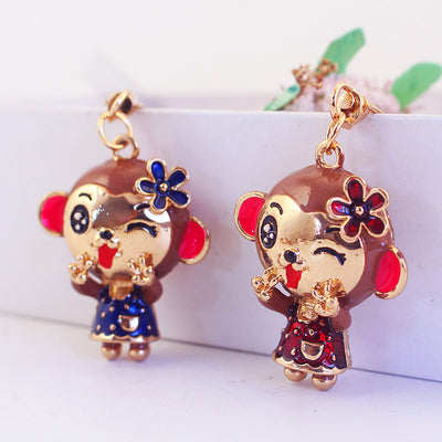 Two winking monkey charms in red and blue dresses beside a white planter.