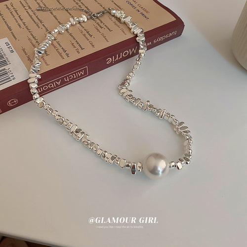 Silver irregular scrap metal pearl necklace on book and white table