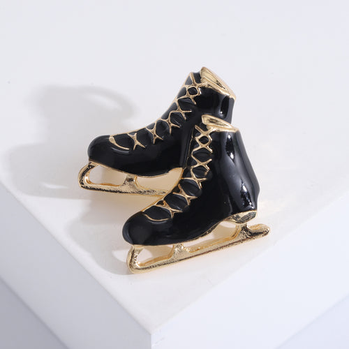 Black enamel ice skate pair brooch close-up on white block