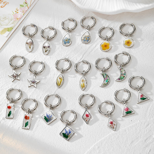 Many silver huggie hoops with geometric dried flower resin charms in mixed shapes