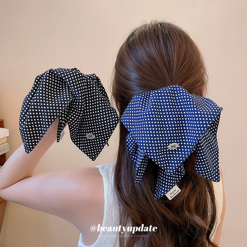 Woman wearing navy polka bow scrunchie holding black polka bow