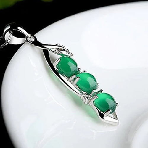 Close-up of green cabochon pea pod pendant on white dish