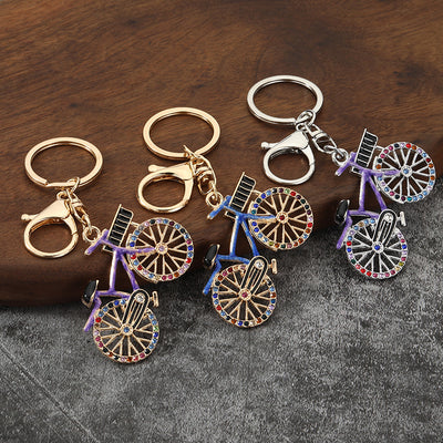 Four bicycle keychains with blue, purple, and white frames in gold-tone and silver-tone finishes.