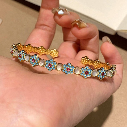 Gold open cuff blue enamel flowers white cabochons held in palm