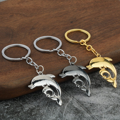 Three dolphin pair keychains displayed in silver, gunmetal, and gold-tone finishes.