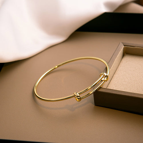 Gold expandable wire bangle on brown surface beside jewelry box