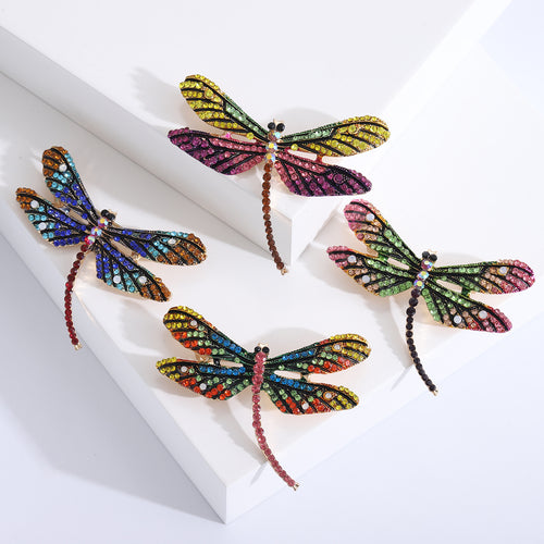 Angled display of the multicolor dragonfly brooch on a white surface