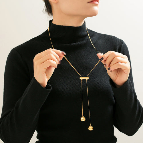 Hands adjusting gold snake-chain lariat with bar and ball drops