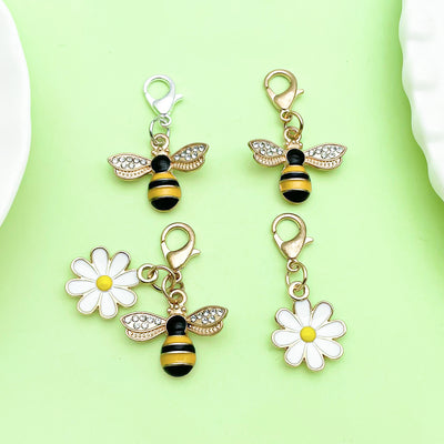 Four bee and daisy lobster clasp charms arranged on a green background.