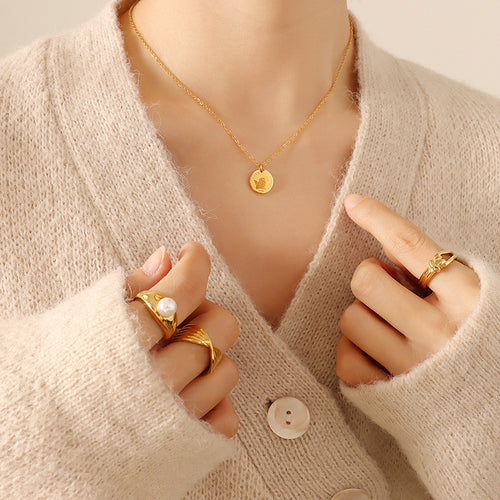 Gold angel coin pendant necklace worn on beige cardigan