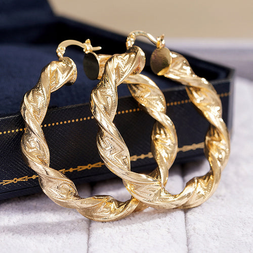 Gold engraved twist hoop earrings on dark jewelry box