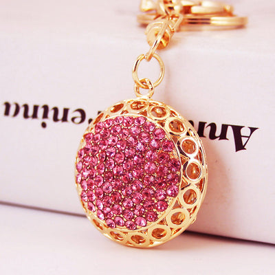 Close-up of a pink rhinestone round pendant hanging from gold-tone keychain hardware.