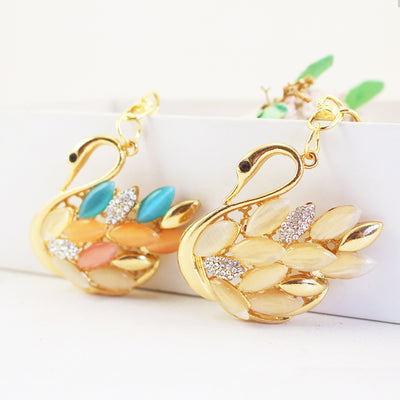 Two swan keychains display white and multicolored oval inlays in gold-tone frames.