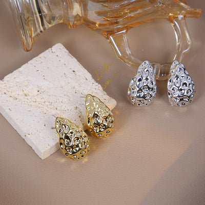 Gold and silver textured teardrop studs on stone and beige surface