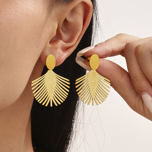 Model adjusting gold palm leaf drop earrings near ear