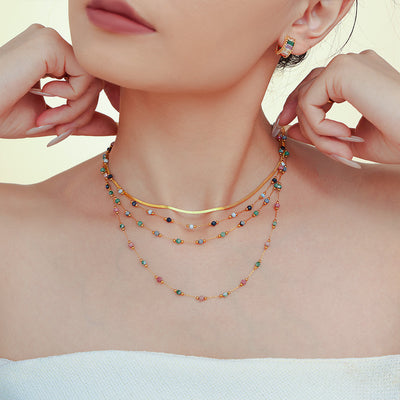 Model wearing layered gold snake chain and multicolor natural stone station necklaces