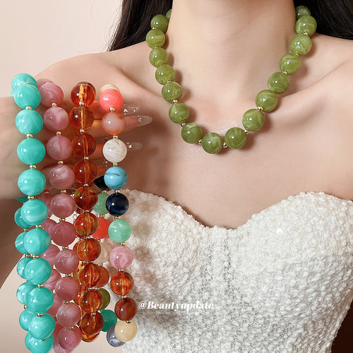 Woman wearing olive green round bead necklace holding multicolor aqua pink amber strands
