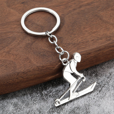 Silver-tone skiing athlete keychain resting on a wooden surface.