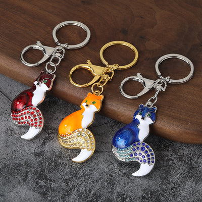 Three fox keychains in red, orange and blue with gold-tone and silver-tone fittings on a wooden surface.