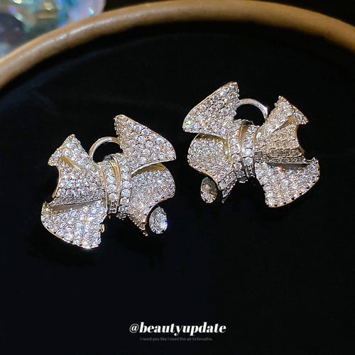 Silver Tone Crystal Crinkle Bow Statement Stud Earrings arranged to show the overall design