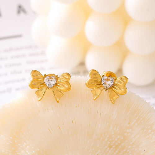 Pair of gold heart-glass bow studs on cream shell surface