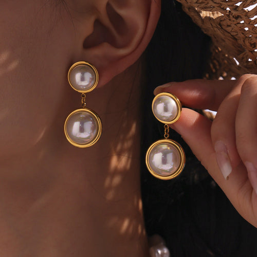 Model holding matching gold double pearl drop earring