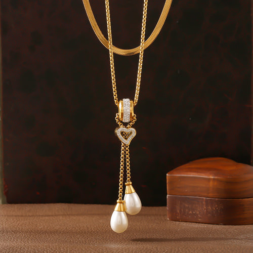 Close-up of gold pearl heart drop necklace with snake chain on dark brown backdrop