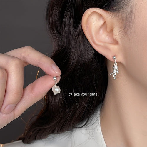 Jellyfish earring worn on ear while holding matching pearl stud