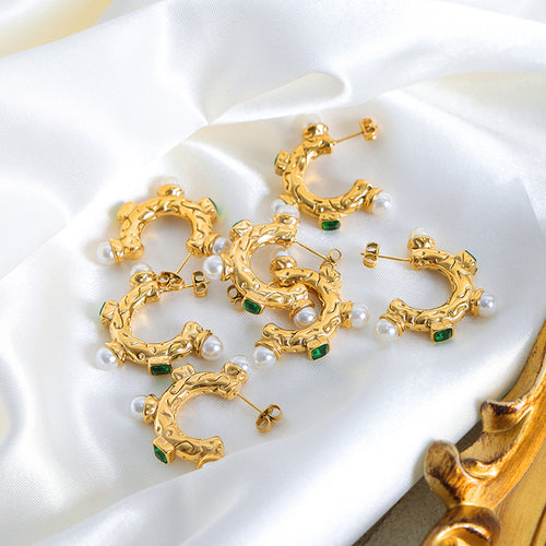 Multiple gold C hoop pearl green stone earrings on white fabric