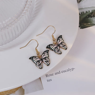 Pink black butterfly drop earrings on white plate with text card
