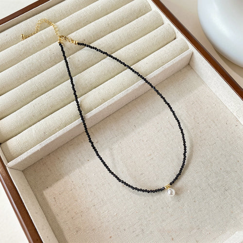 Styled wear view of 黑色串珠珍珠项链 showing a slim strand of tiny black beads centered by one small white pearl drop