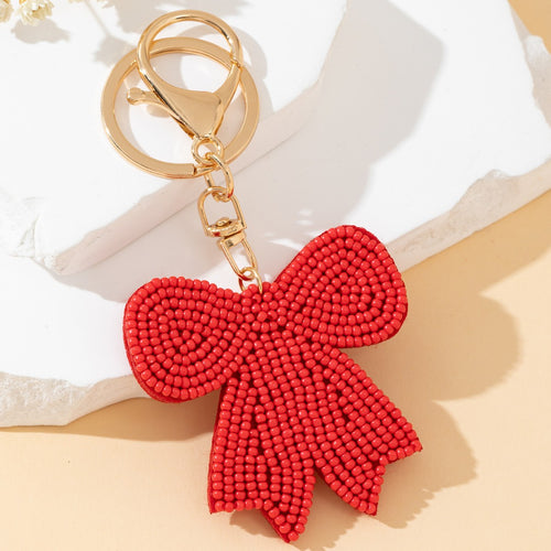 Close-up of the red seed bead bow charm hanging from a gold lobster clasp