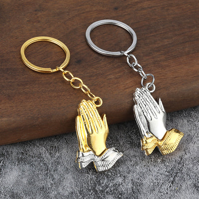 Silver-hands and gold-hands keychains displayed together on a wooden surface.