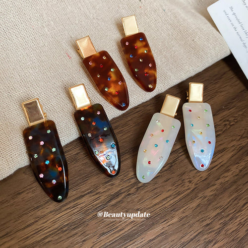several brown and white crystal teardrop clips arranged on wood