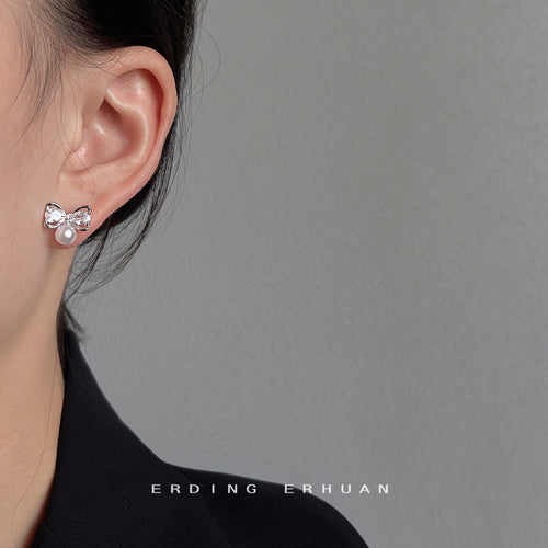 Silver-tone clear-butterfly white-pearl-like studs shown worn on an ear.